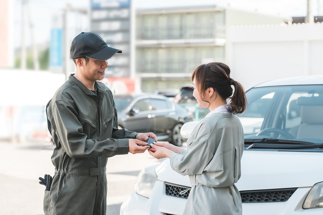 女性客に車の鍵を渡す自動車整備士