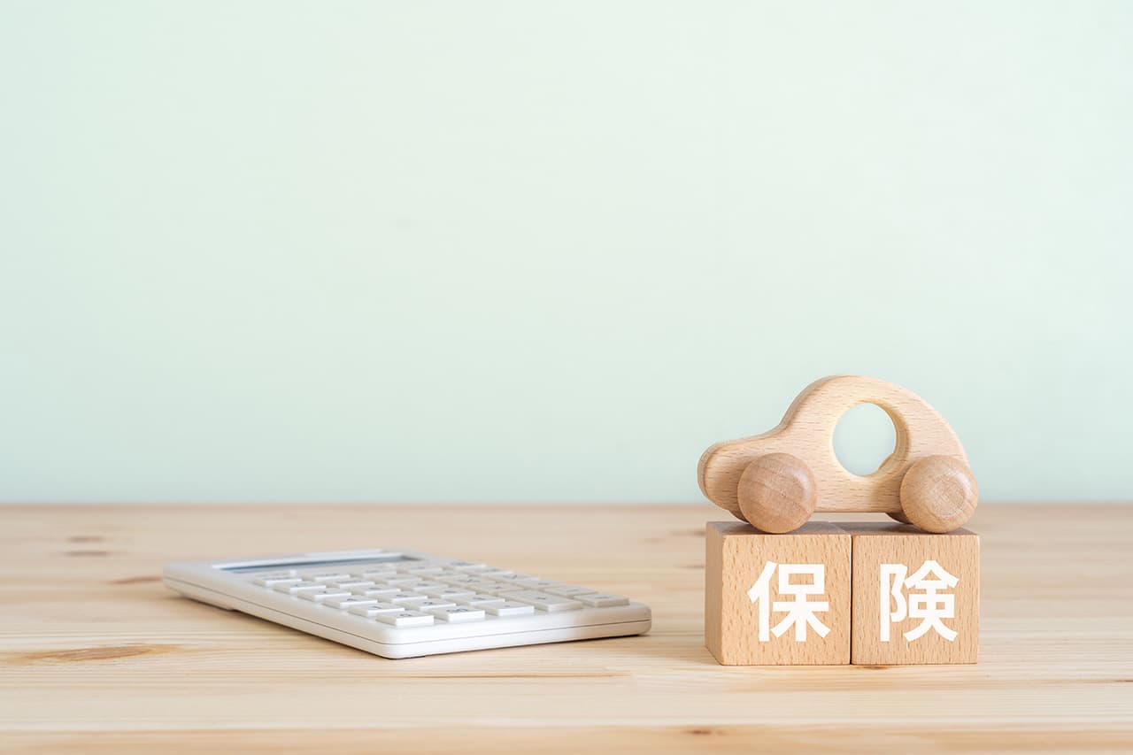 保険と書かれた木のブロックと電卓と木の車の模型